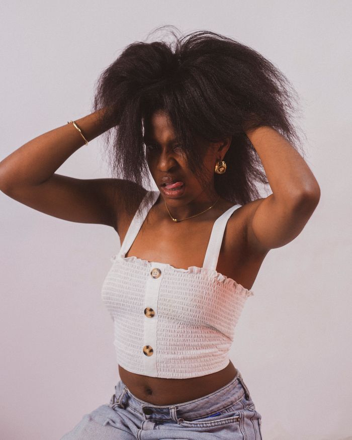 Portrait of a young woman with natural hair showing frustration indoors, wearing a stylish top.